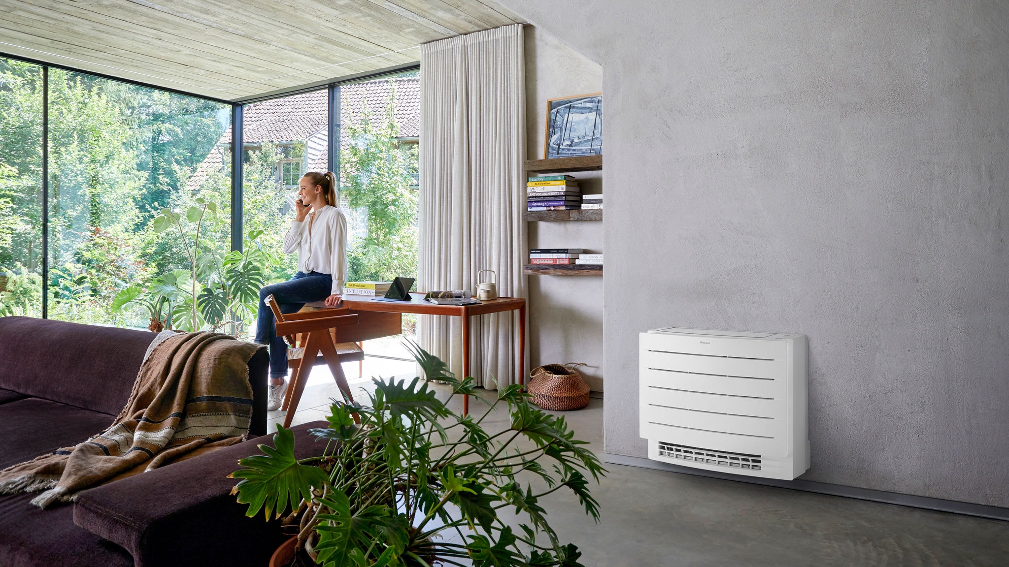 Femme au téléphone, appuyée sur son bureau et profitant d'un climat confortable dans son salon grâce à une unité console posée au sol.