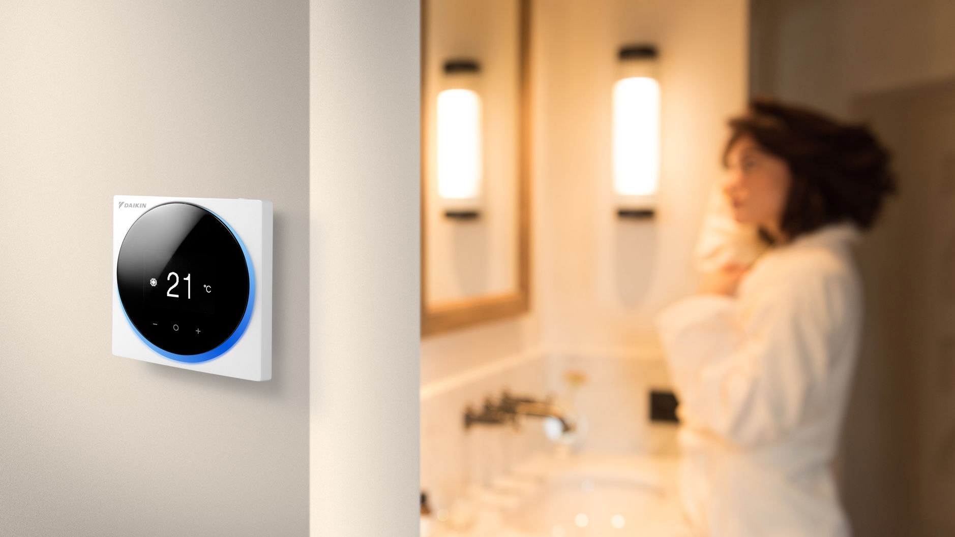 Femme debout dans une salle de bains à côté d'une chambre équipée d'un thermostat d'ambiance compact filaire fixé au mur